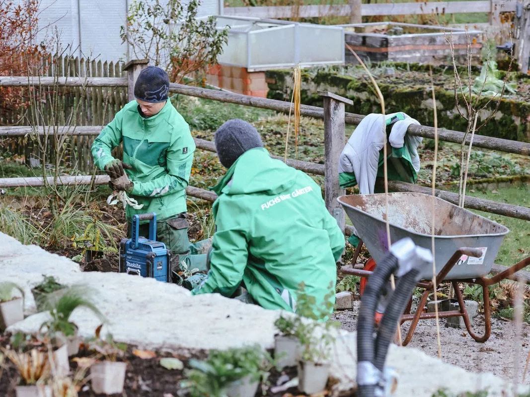 Kollegen in grüner Arbeitskleidung arbeiten in den Staudenbeeten an der Kalksteinmauer